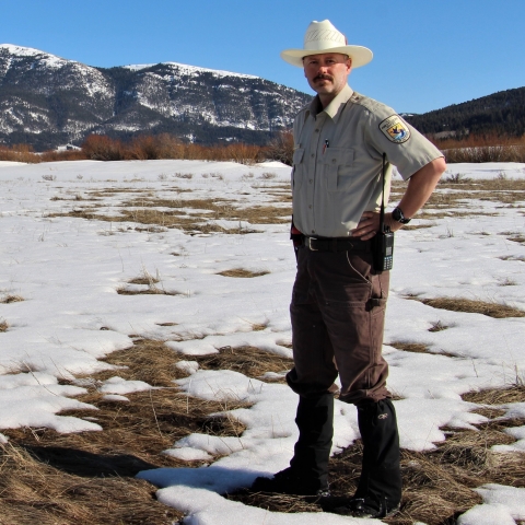 District Manager Cortez Rohr in a field of melting snow under blue skies with mountains in the background.